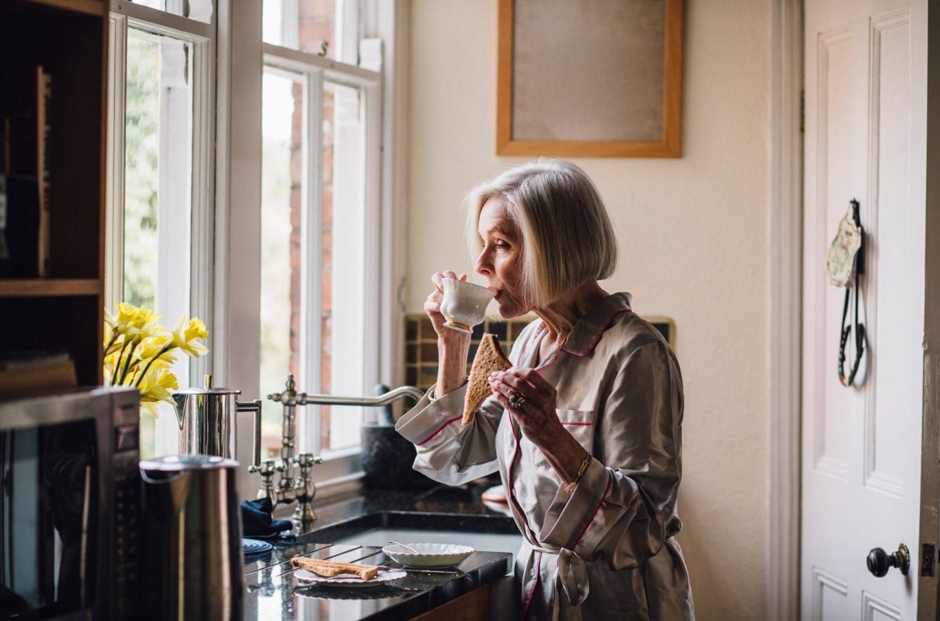 Retired woman drinking coffee alone in the morning in the kitchen wondering what to do with her time.